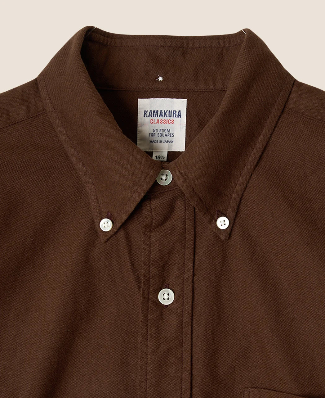 Close-up of a brown Kamakura Classics button-down shirt collar with white buttons and a visible brand label.
