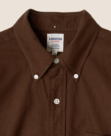 Close-up of a brown Kamakura Classics button-down shirt collar with white buttons and a visible brand label.