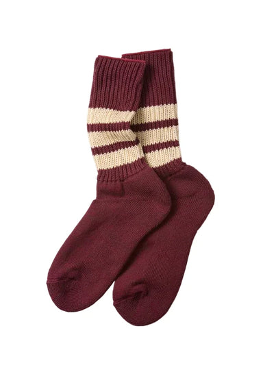 A pair of maroon crew socks with cream and maroon horizontal stripes near the ribbed cuffs, displayed on a light gray background.
