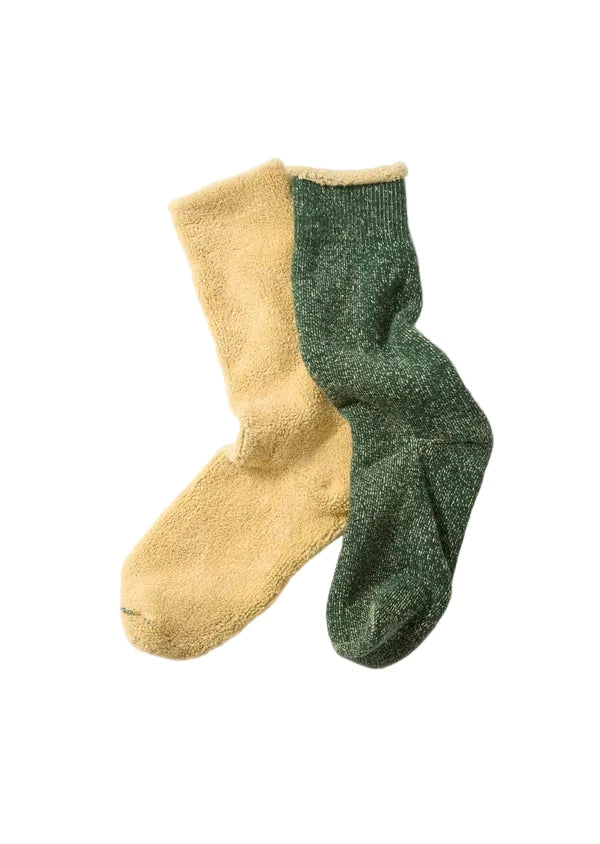 A pair of split-color socks, with one half in a soft mustard yellow and the other half in a heathered dark green, laid flat on a light gray background.
