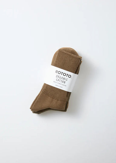 A pair of brown cotton crew socks rolled up with a white paper band labeled 'ROTOTO ORGANIC COTTON', photographed on a clean white background.