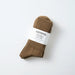 A pair of brown cotton crew socks rolled up with a white paper band labeled 'ROTOTO ORGANIC COTTON', photographed on a clean white background.