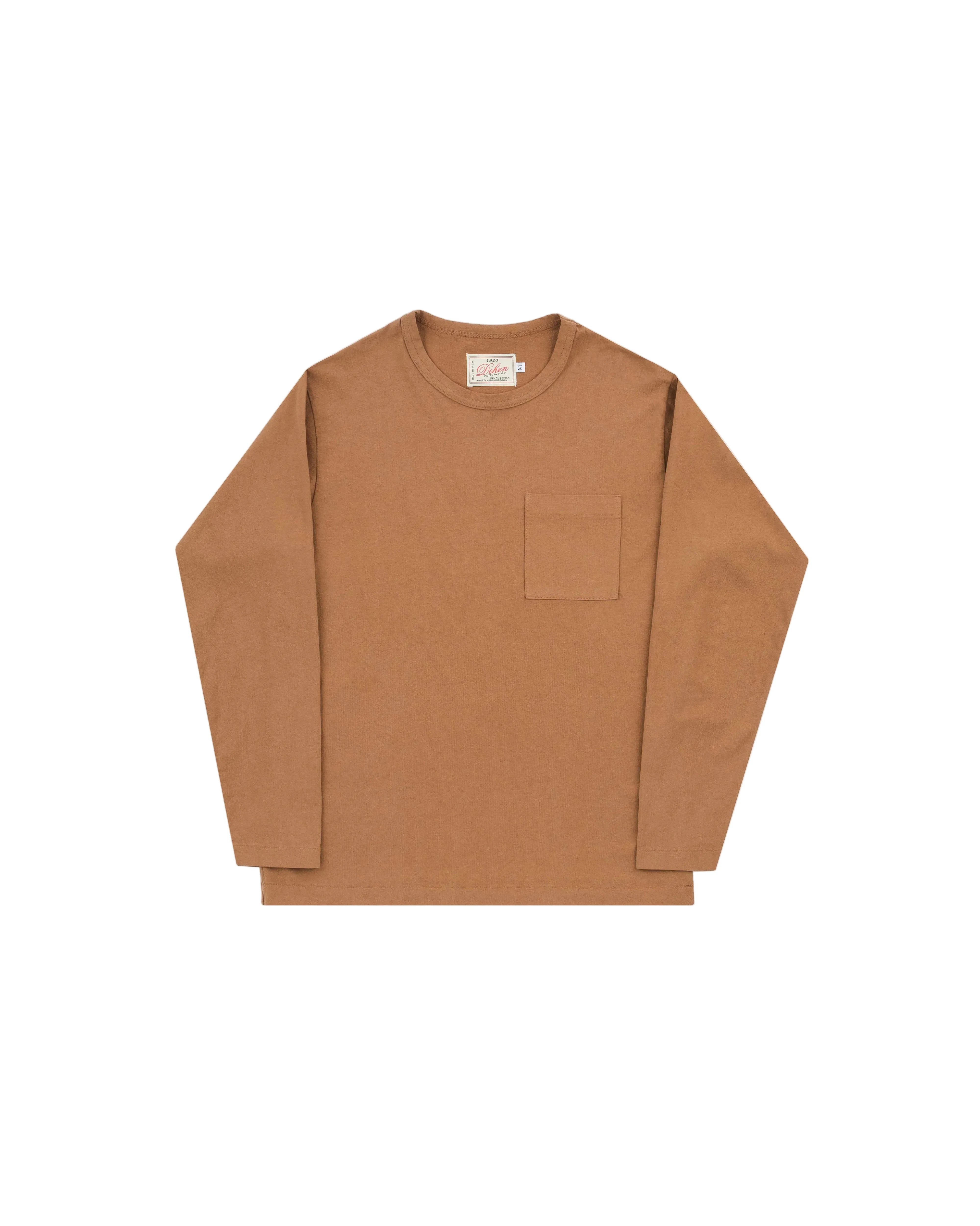 A long-sleeve crewneck shirt in a warm camel brown color, featuring a single patch pocket on the left chest, laid flat against a light gray background.