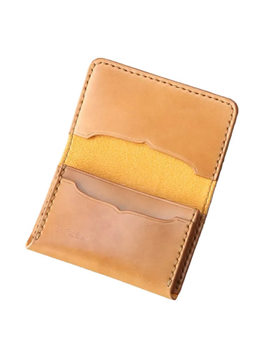 A slim tan leather card holder wallet with multiple card slots, shown open on a rustic gray wooden plank background.