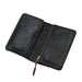 A black leather zip-around wallet with card slots, shown open on a rustic wooden plank surface. The brand name 'THE PLAYMATE' is debossed on the left card slot panel.