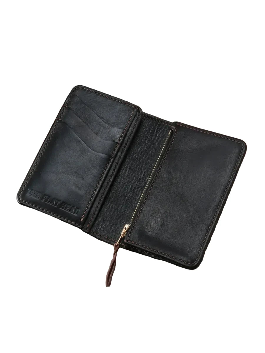 A black leather zip-around wallet with card slots, shown open on a rustic wooden plank surface. The brand name 'THE PLAYMATE' is debossed on the left card slot panel.