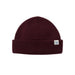 A dark burgundy ribbed knit beanie hat with a small white rectangular brand tag on the side, displayed against a clean off-white background.