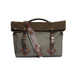 A rugged canvas and wool bag in olive green and brown, featuring dark brown leather straps with brass buckles and a top handle, set against a plain off-white background.
