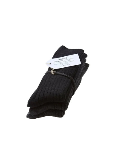 A pair of black ribbed knit socks bundled with a white paper tag and a small gold ring, photographed on a clean white background.